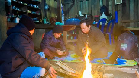 Men huddle around a smartphone by a fire in a hut